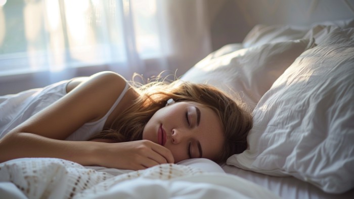 Femme dormant paisiblement sur le côté avec les écouteurs Ozlo Sleepbuds dans un lit confortable