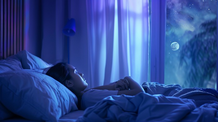 Personne dormant paisiblement dans une chambre baignée de lumière lunaire douce, évoquant un sommeil réparateur