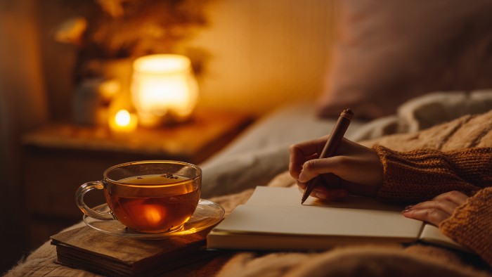 Femme écrivant dans son journal le soir avec une lumière douce et une tisane, créant un rituel apaisant avant le coucher