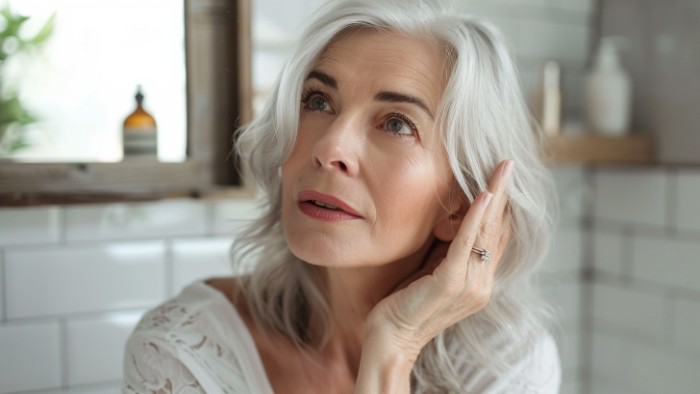 Femme de 50 ans aux cheveux blancs dans sa salle de bain regardant son reflet avec précaution avant application de Bétadine